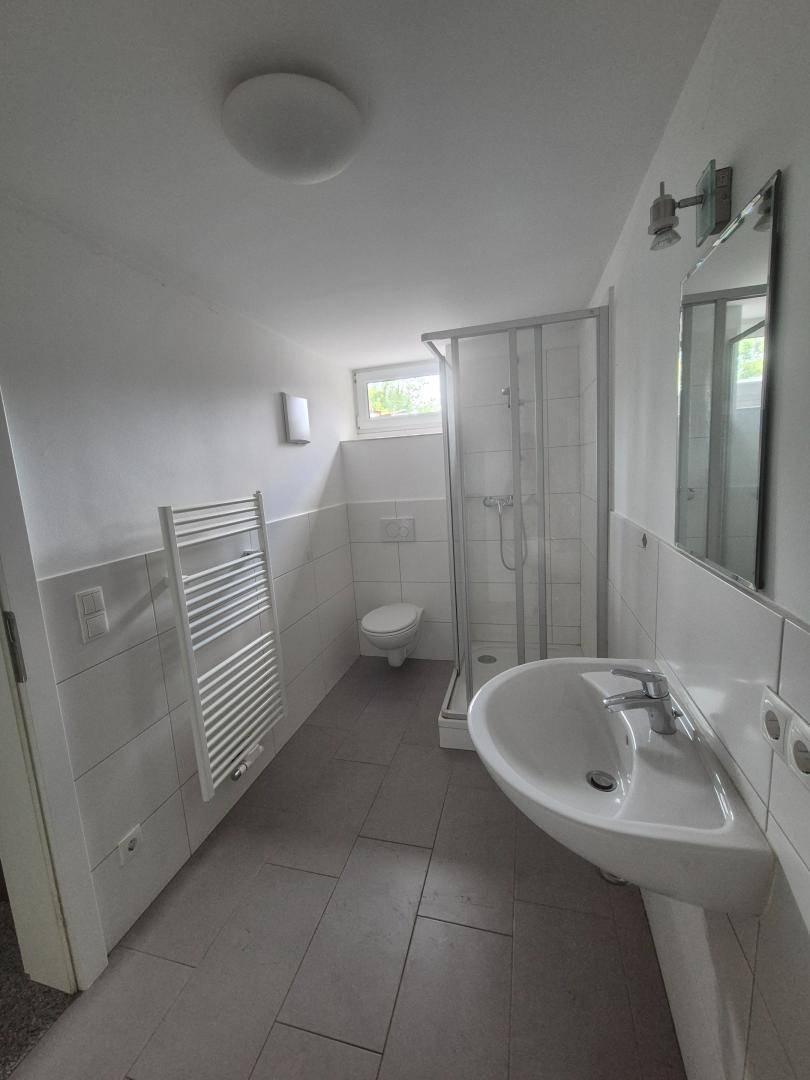 Helles Badezimmer mit Dusche, WC, Waschtisch, beheiztem Handtuchhalter und Fenster.