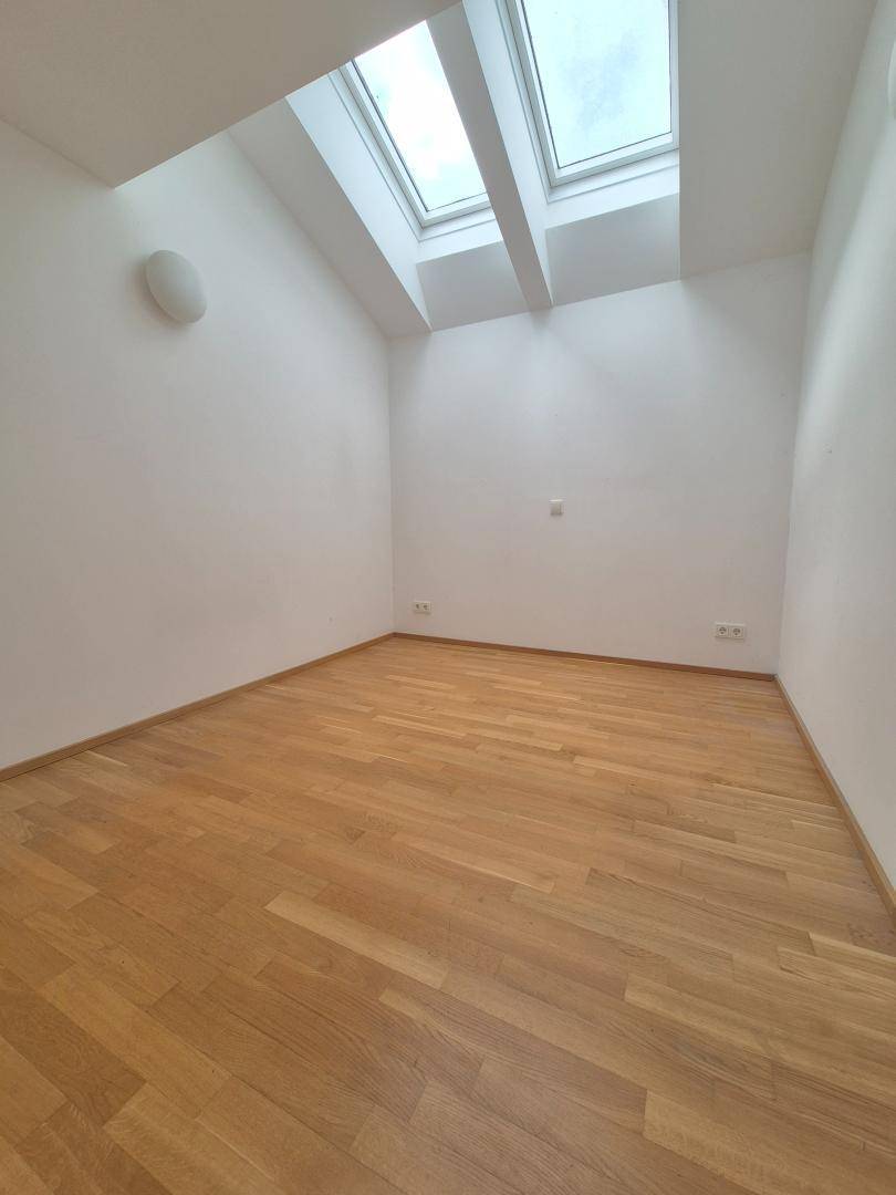 Kleines Zimmer mit Parkettboden und zwei Dachfenstern, bietet viel natürliches Licht.