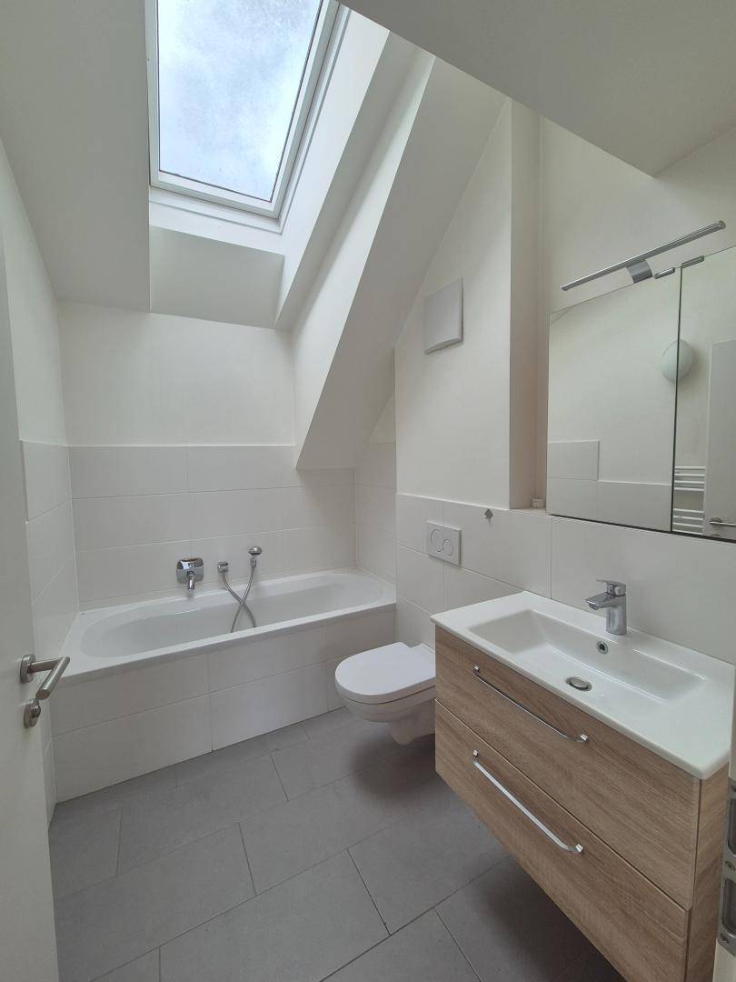 Modernes Badezimmer mit Badewanne, WC, Waschtisch und Dachfenster für natürliches Licht.