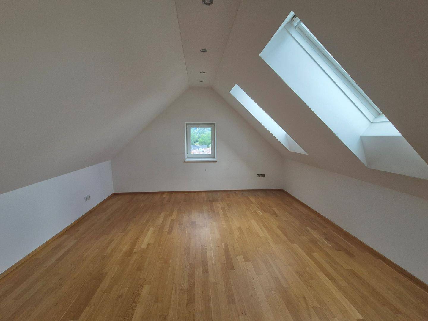 Geräumiges Dachzimmer mit Parkettboden, Dachfenstern und Einbaustrahlern in der Decke.