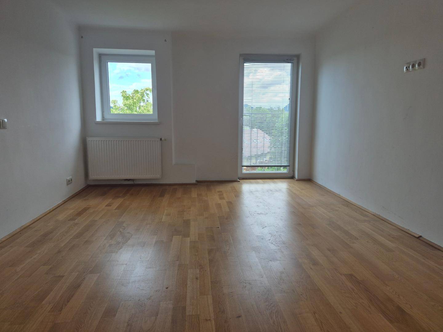Helles Zimmer mit Parkettboden, Fenster und Tür mit Jalousien, ideal als Schlaf- oder Arbeitszimmer.