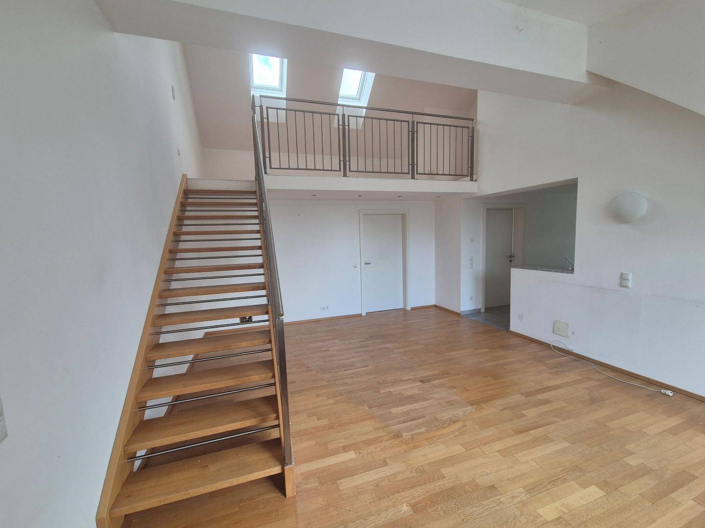 Geräumiges Wohnzimmer mit offener Holztreppe und Blick auf die obere Galerie mit Dachfenstern.