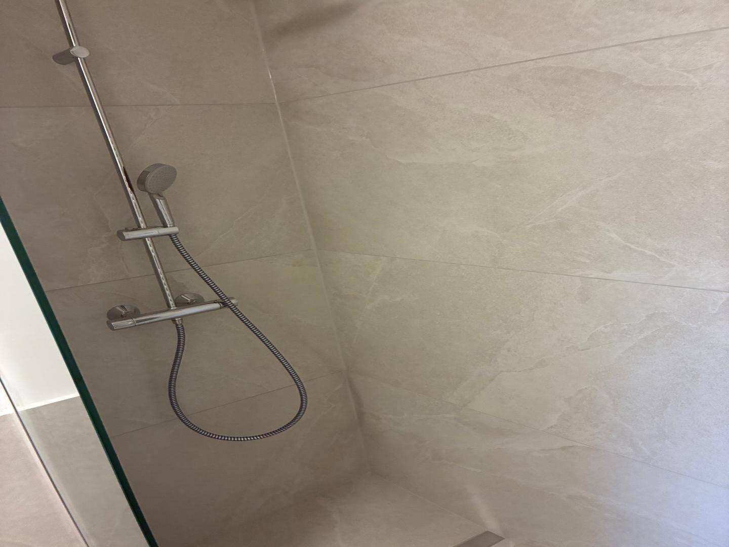 Nahaufnahme der Duscharmatur und der großformatigen Fliesen in der begehbaren Dusche.