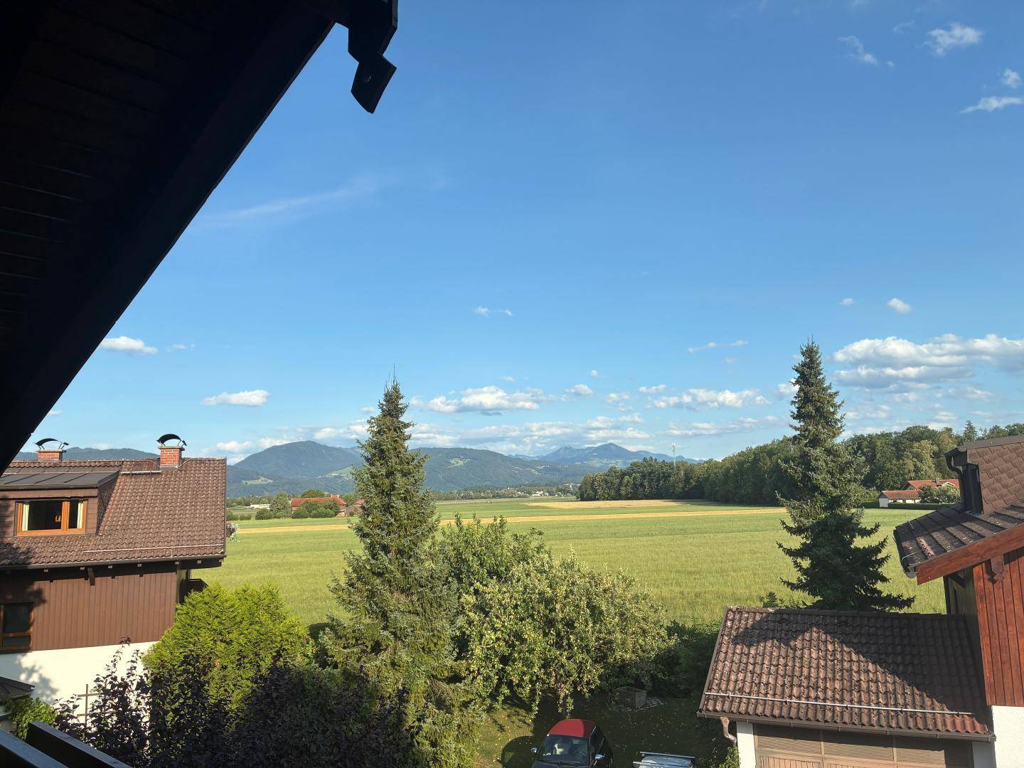 Weitläufiger Blick vom Balkon über grüne Felder und die umliegende Berglandschaft.