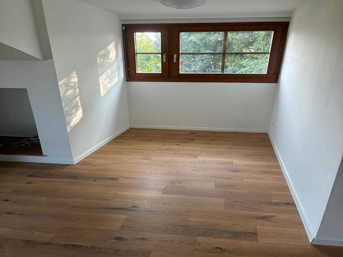 Sonniges Dachzimmer mit warmem Holzboden und schrägen Wänden, bereit zur individuellen Gestaltung.