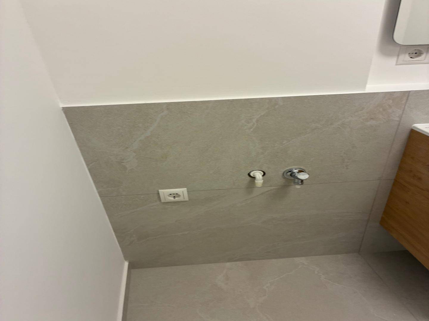Detailansicht der modernen grauen Fliesenwand im Badezimmer mit Anschlüssen.
