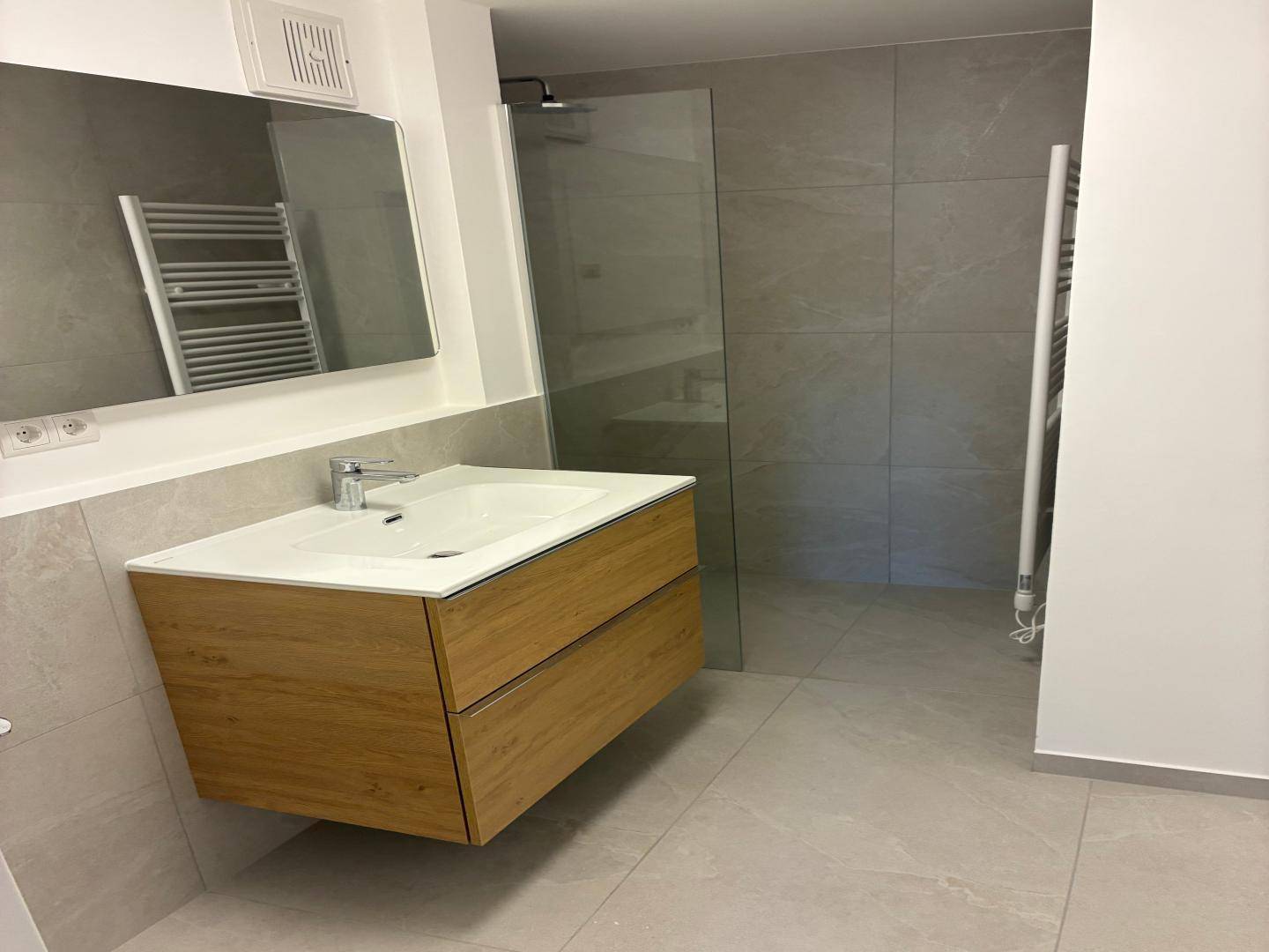 Modernes Badezimmer mit schwebendem Waschtisch, begehbarer Dusche und beheiztem Handtuchhalter.