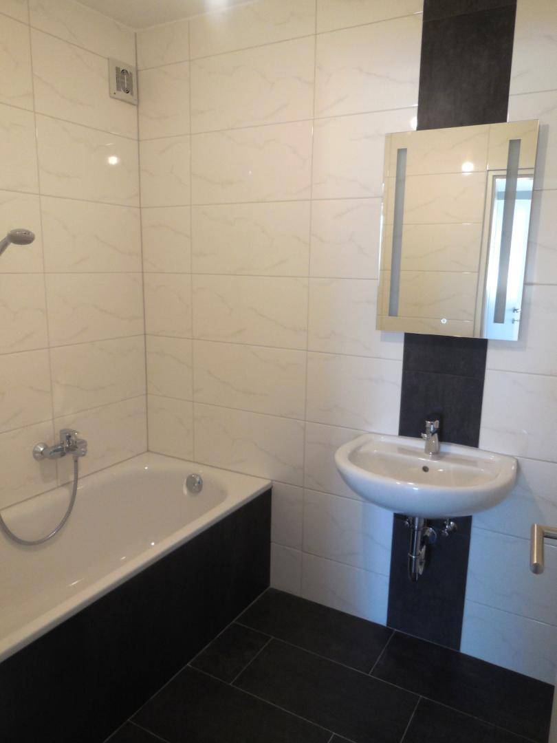 Modernes Badezimmer mit Badewanne, Waschbecken und einem Spiegel, gestaltet mit weißen und schwarzen Fliesen.