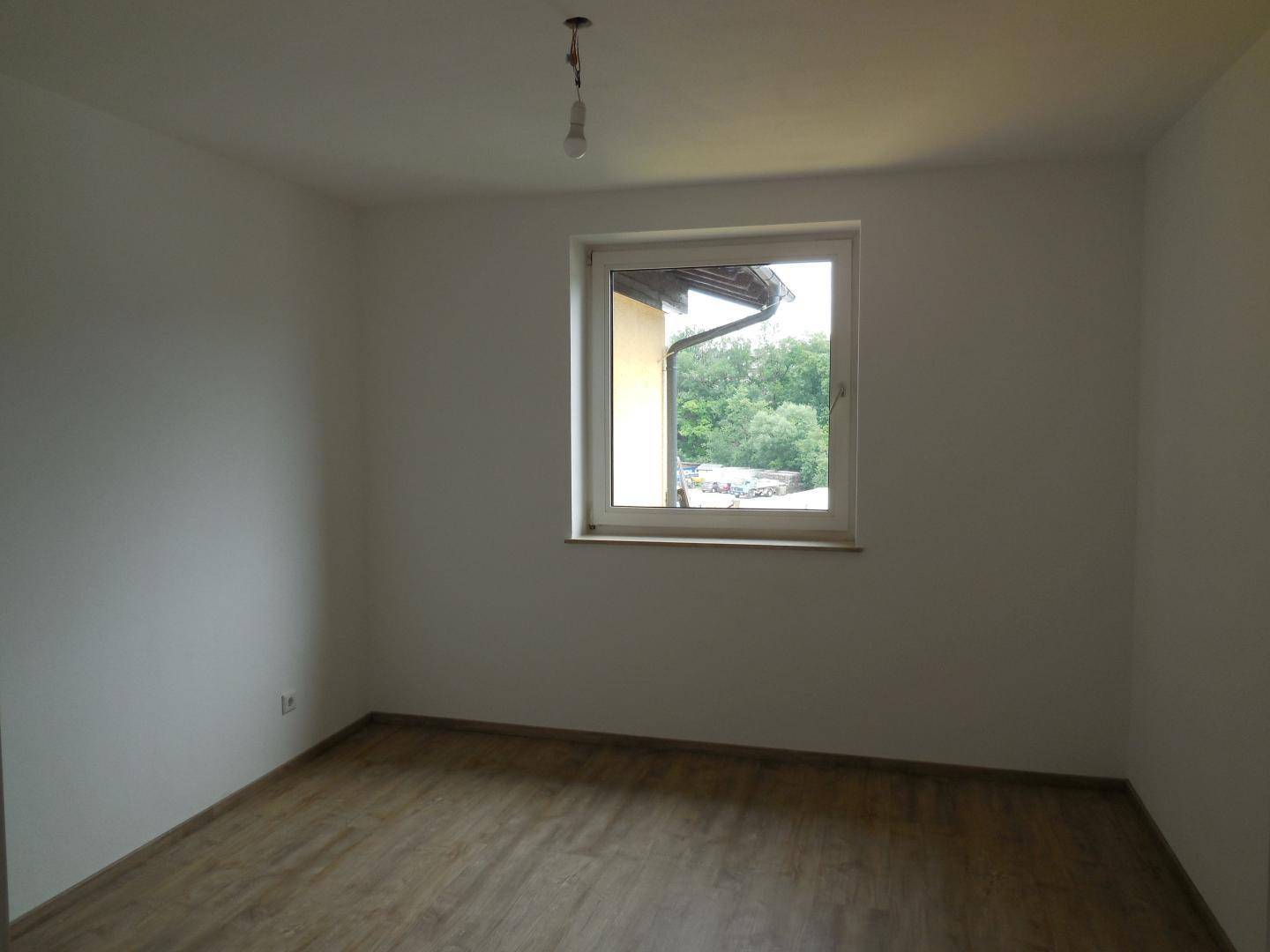 Leeres Zimmer mit Laminatboden und weiß gestrichenen Wänden, bietet einen ruhigen Blick ins Grüne.