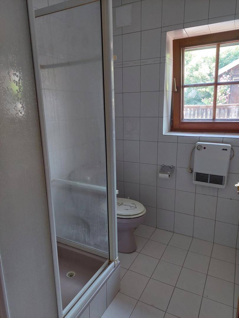 Badezimmer mit Duschkabine, WC, Fenster und weißen Fliesen.