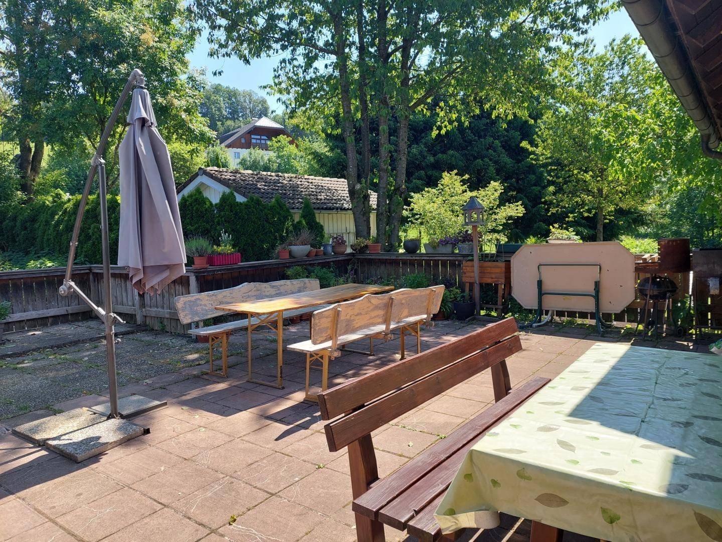 Geräumige Außenterrasse mit Sitzgelegenheiten und Sonnenschirm, umgeben von viel Grün.