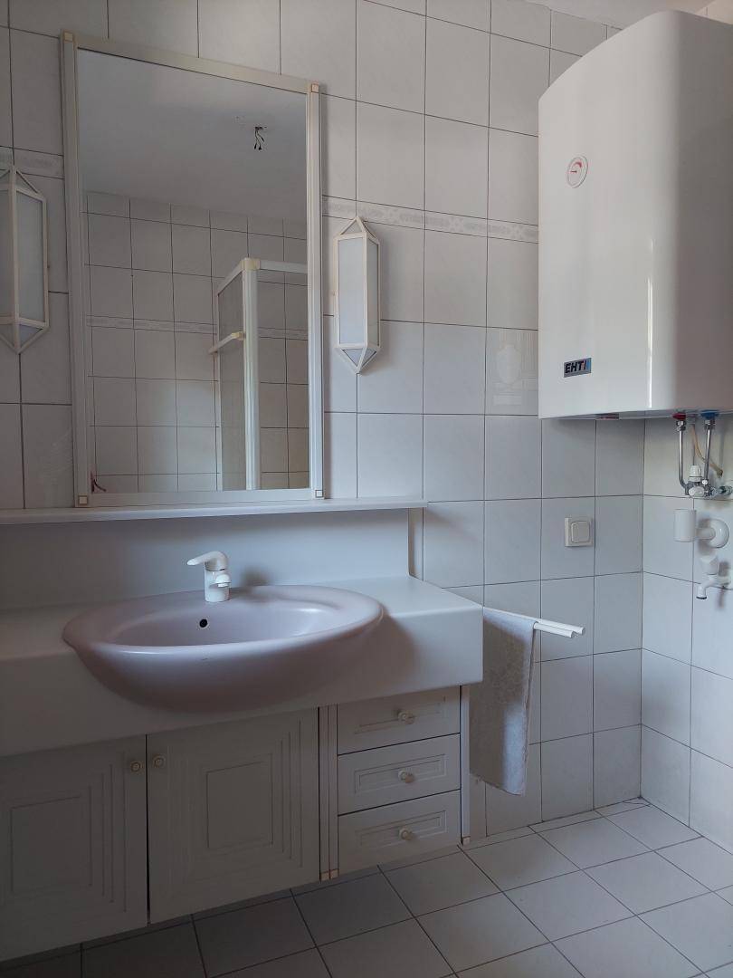 Helles Badezimmer mit Waschbecken, Spiegel und Wandboiler, komplett gefliest.