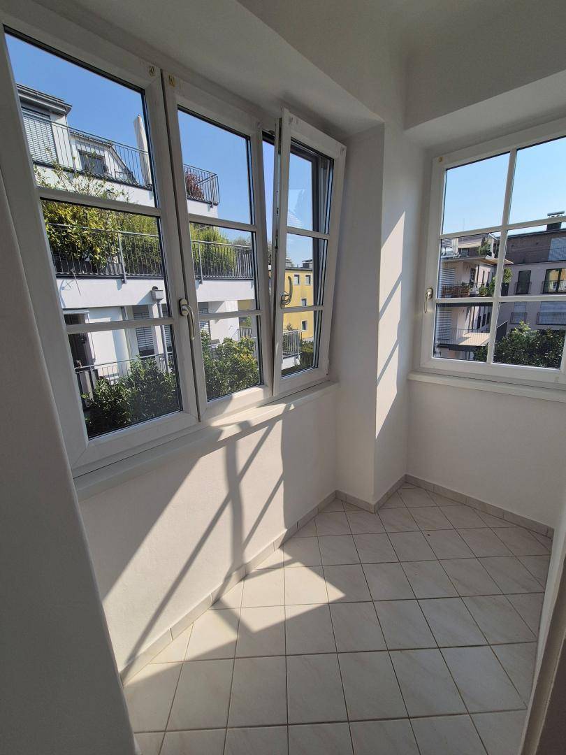 Sonnige Loggia mit Fliesenboden und Blick auf die umliegenden Gebäude und Bäume.