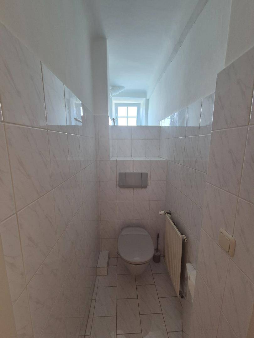 Kleines Gäste-WC mit weißen Fliesen, wandhängendem WC und einem Fenster für Tageslicht.