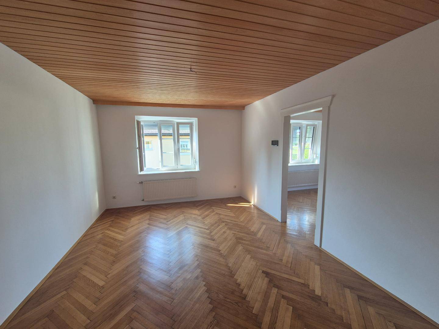 Geräumiges Zimmer mit klassischem Fischgrätparkett und einer warmen Holzpaneeldecke.