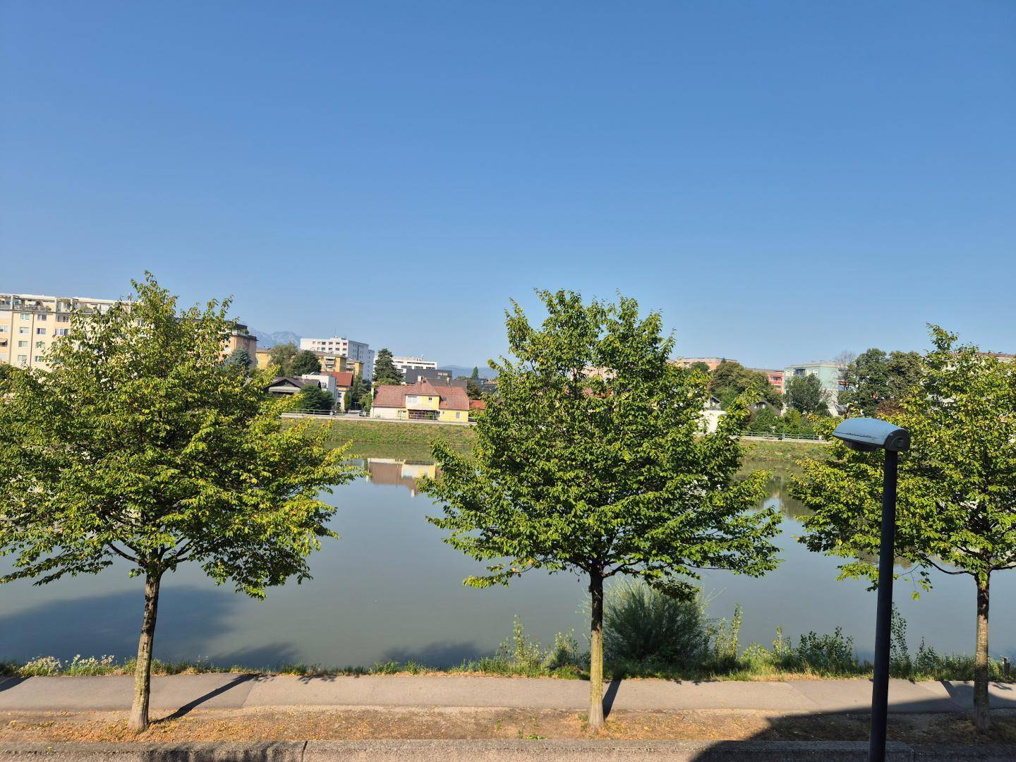 Malerischer Blick auf einen See oder Fluss mit Bäumen und Gebäuden am Ufer.