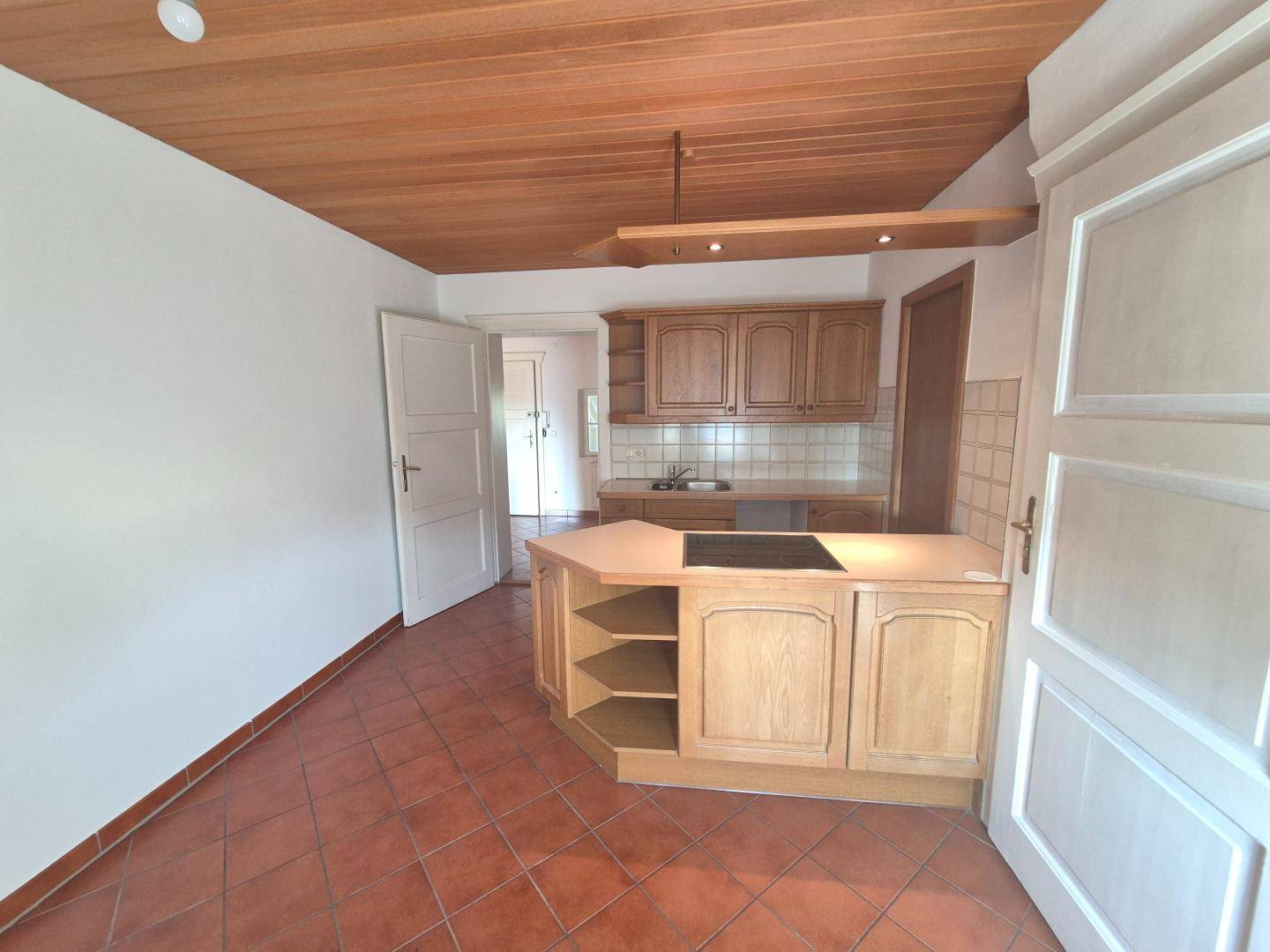 Küche mit Holzschränken, Terrakottafliesen und integriertem Kochfeld unter einer Holzdecke.