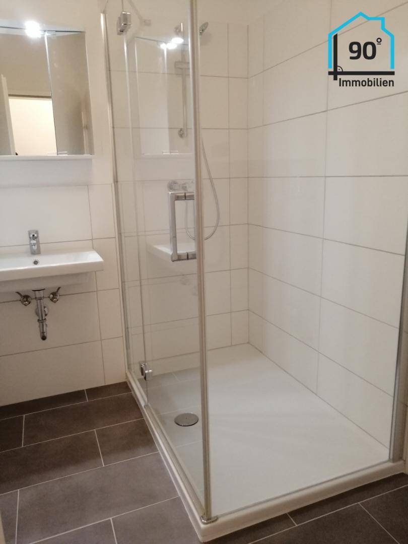 Modernes Badezimmer mit Duschkabine, weißen Wandfliesen und dunklem Boden, in sehr gutem Zustand.