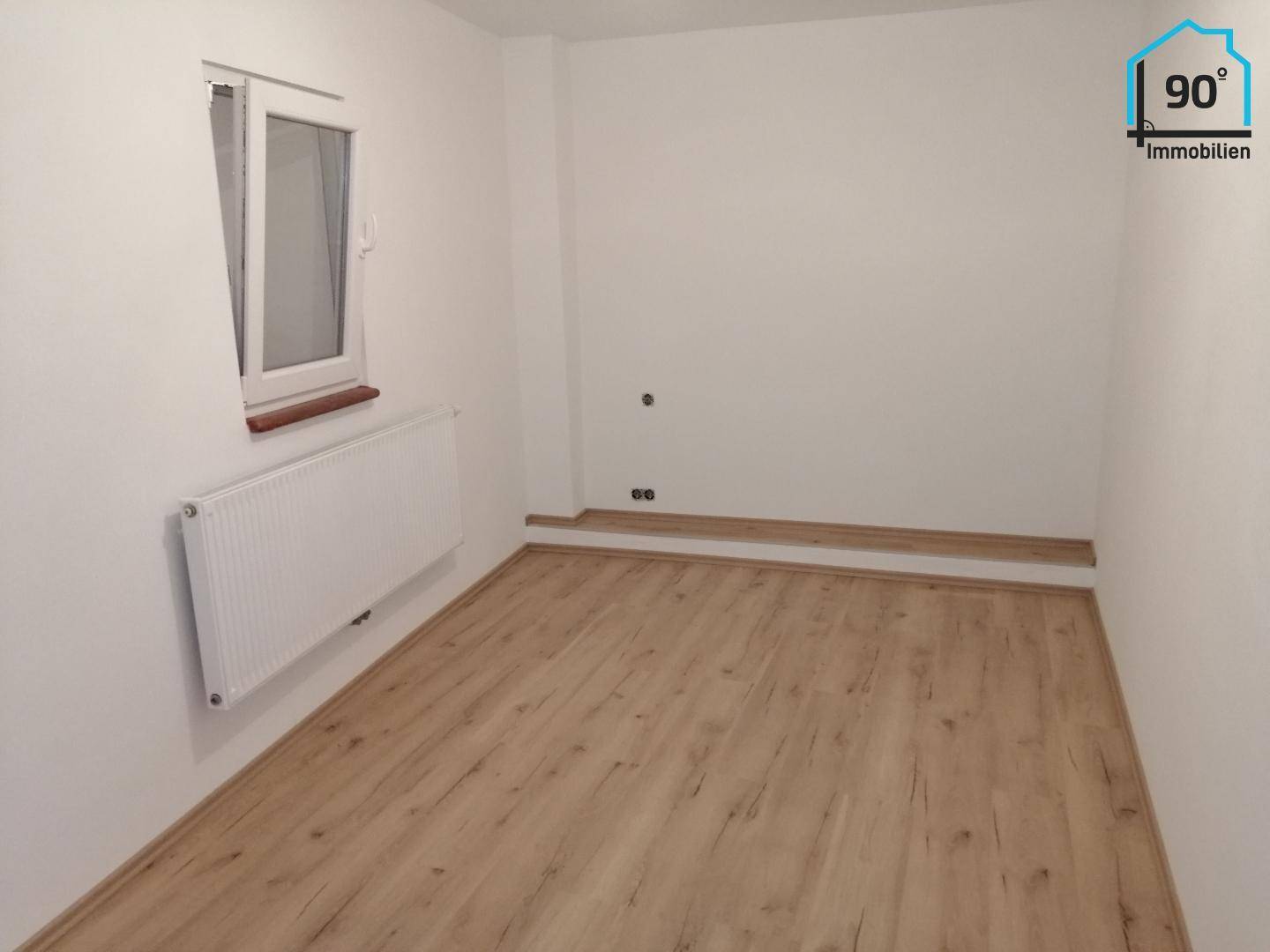 Heller Raum mit Laminatboden, Fenster und Heizkörper, ideal als Schlaf- oder Kinderzimmer, unmöbliert.