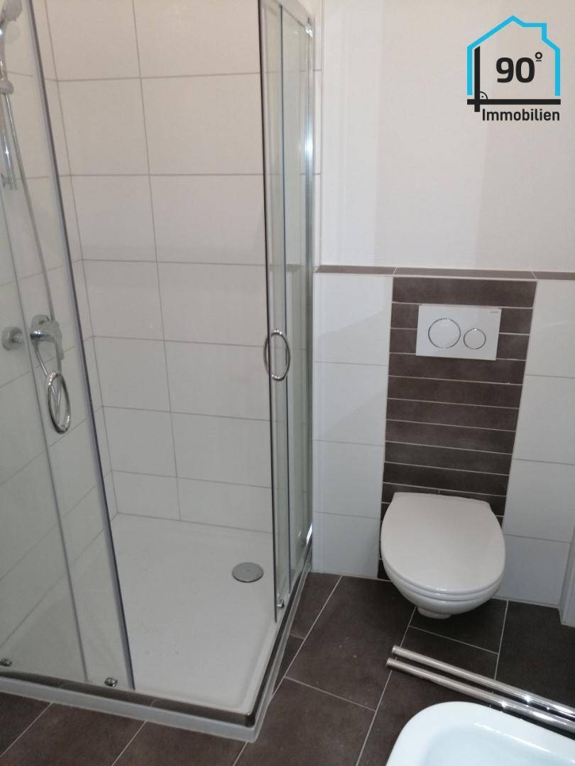 Helles Badezimmer mit Duschkabine und wandhängendem WC, ausgestattet mit modernen Fliesen und Armaturen.