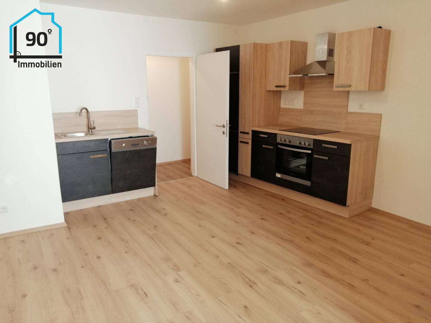 Offener Küchenbereich mit Laminatboden und Einbauküche in Holz- und Anthrazitoptik, bereit zur Nutzung.