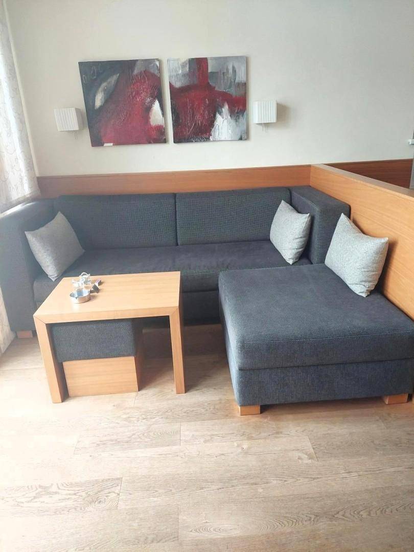 Wohnbereich mit Ecksofa, Couchtisch und Holzboden, dekoriert mit abstrakten Bildern.