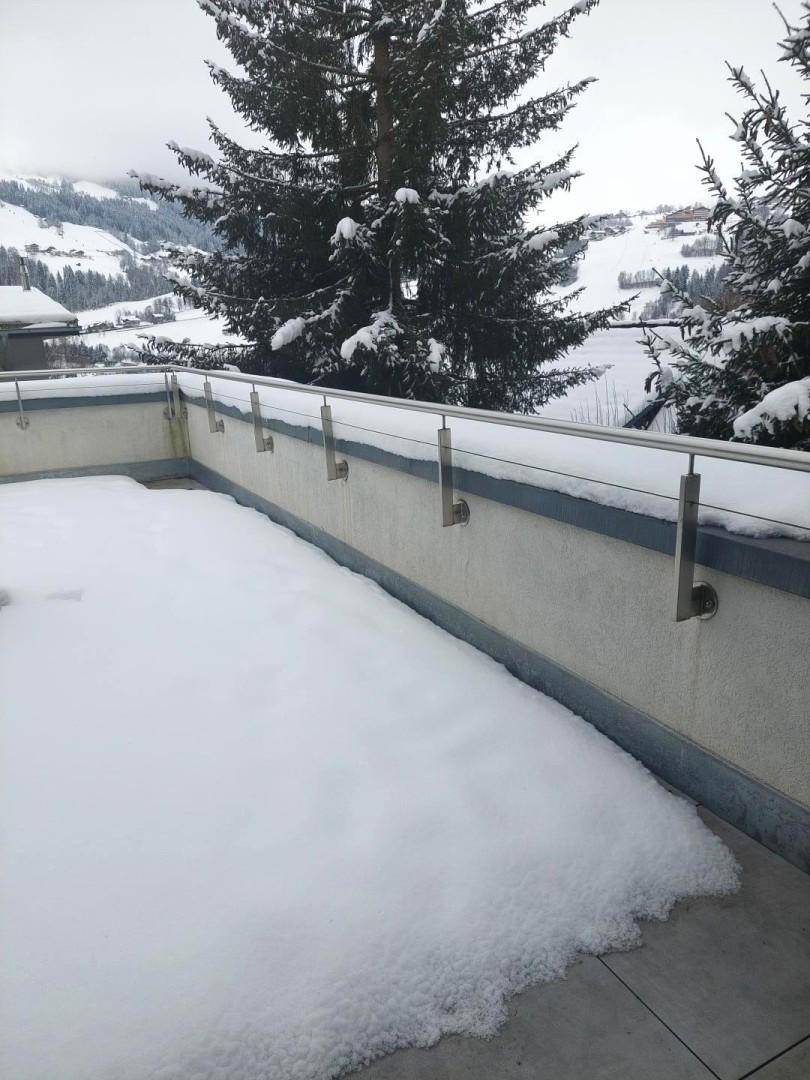Schneebedeckte Terrasse mit Bergblick und Nadelbäumen im Winter.