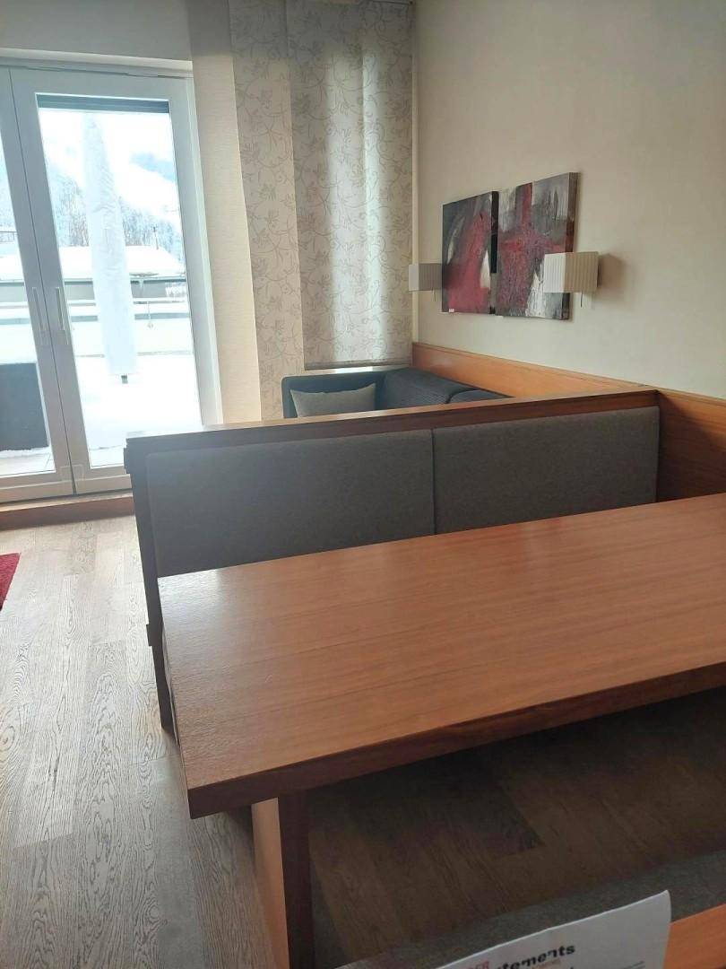 Heller Essbereich mit Holztisch und Sitzbank, angrenzend an einen Wohnbereich mit Balkonzugang.