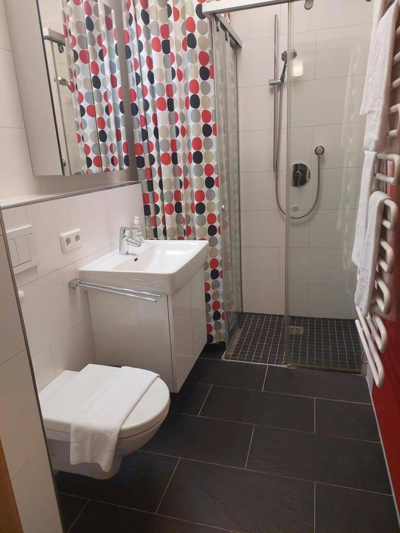 Modernes Badezimmer mit Duschkabine, WC, Waschbecken und farbenfrohem Duschvorhang.
