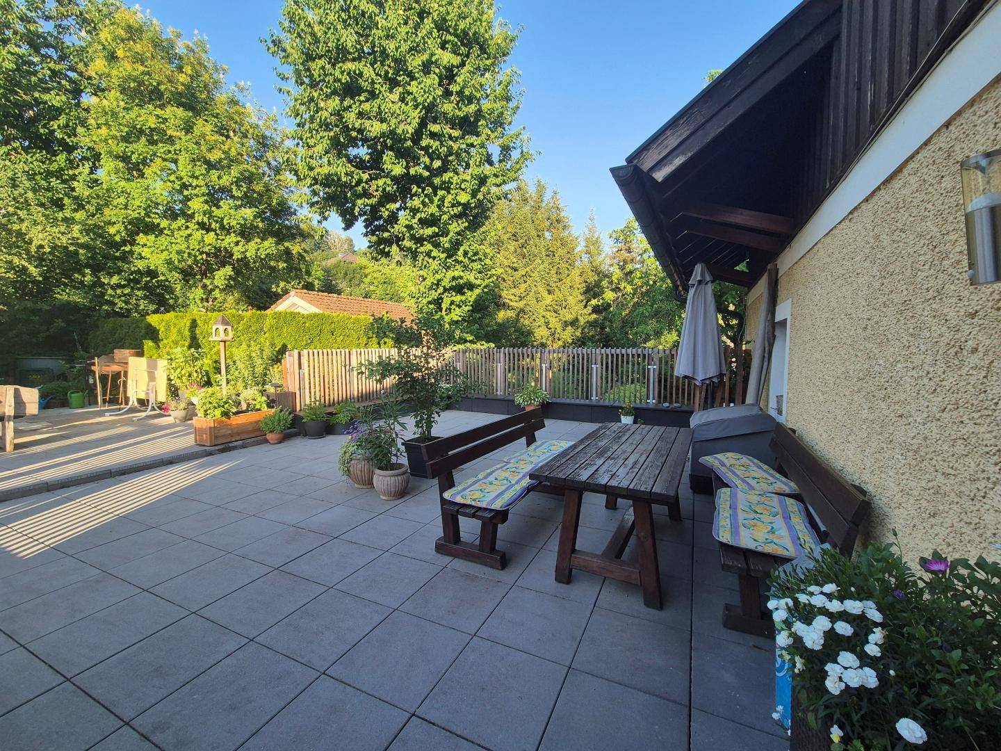 Geräumige Terrasse mit Holzsitzgruppe und viel Grün im Hintergrund, sonnig gelegen.