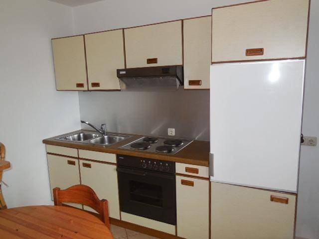 Detailansicht der Küchenzeile mit Herd, Spüle und Kühlschrank in beigen Schränken.