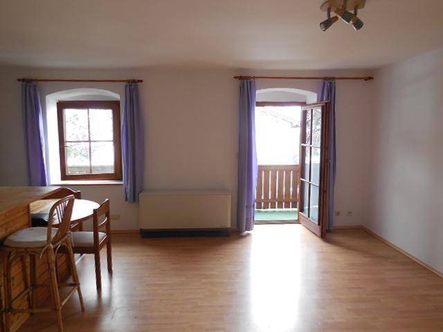 Heller Wohnbereich mit Holzboden und Zugang zu einem Balkon, gut belichtet durch die Tür.