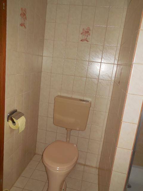 Separate Toilette in einem gefliesten Raum mit beigefarbener Keramik und einfacher Ausstattung.