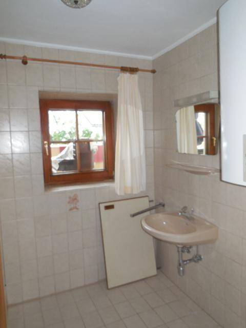 Badezimmer mit Waschbecken, Spiegelschrank und einem Fenster, komplett gefliest.