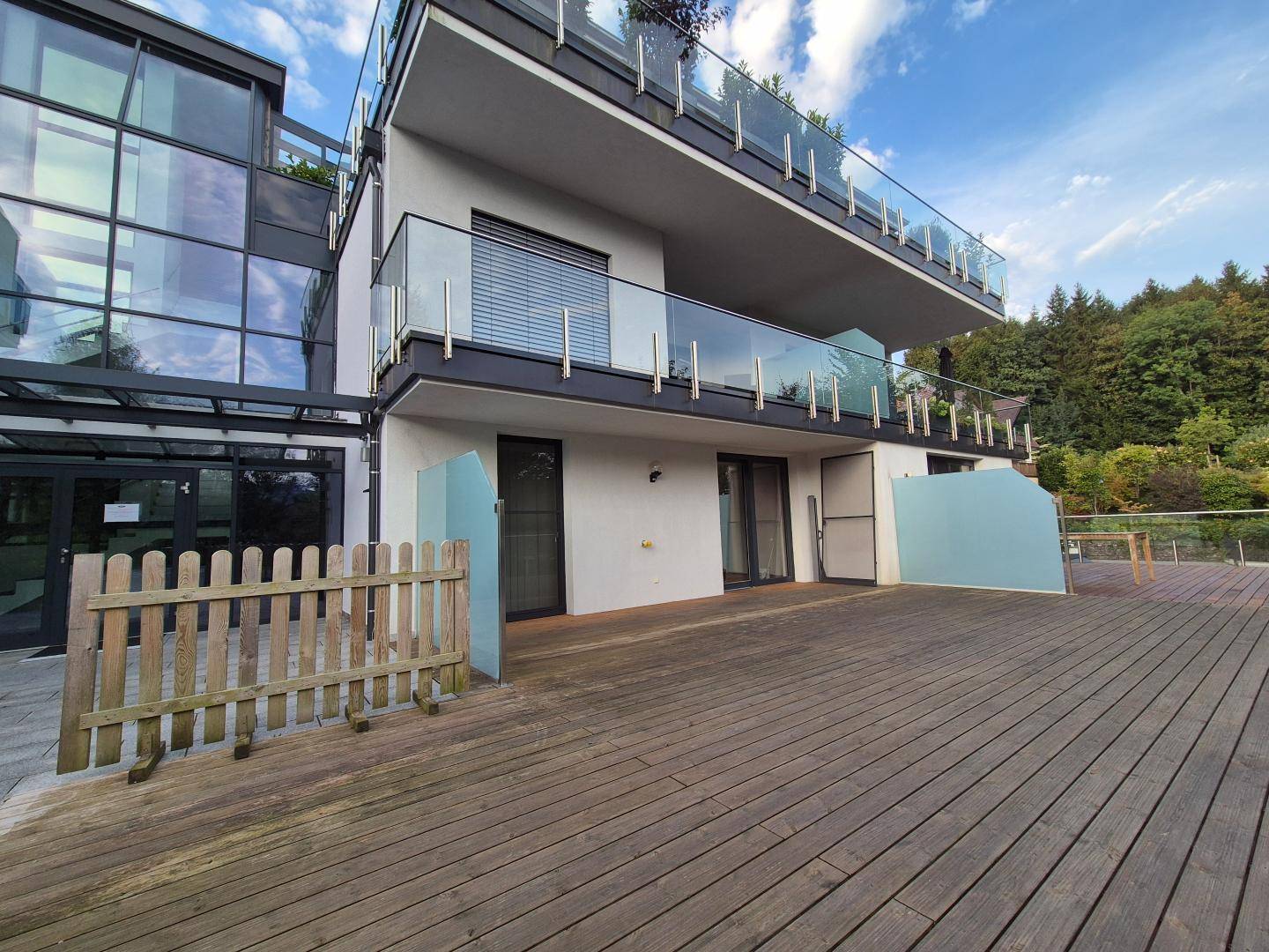Außenansicht des modernen Gebäudes mit weitläufiger Holzterrasse und kleinem Holzzaun.