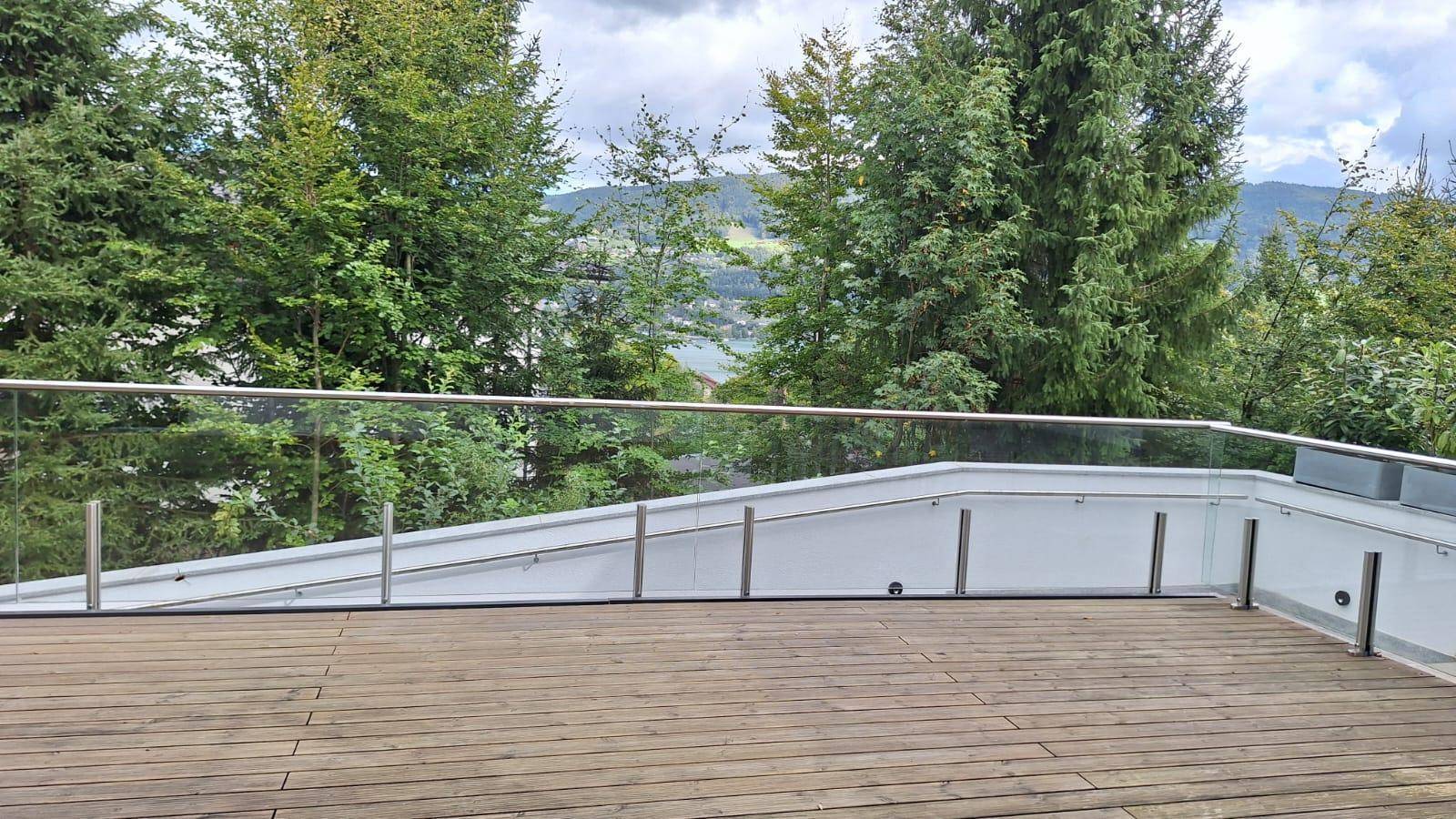 Geräumige Holzterrasse mit Glasgeländer und malerischem Blick auf den See und die Berge.