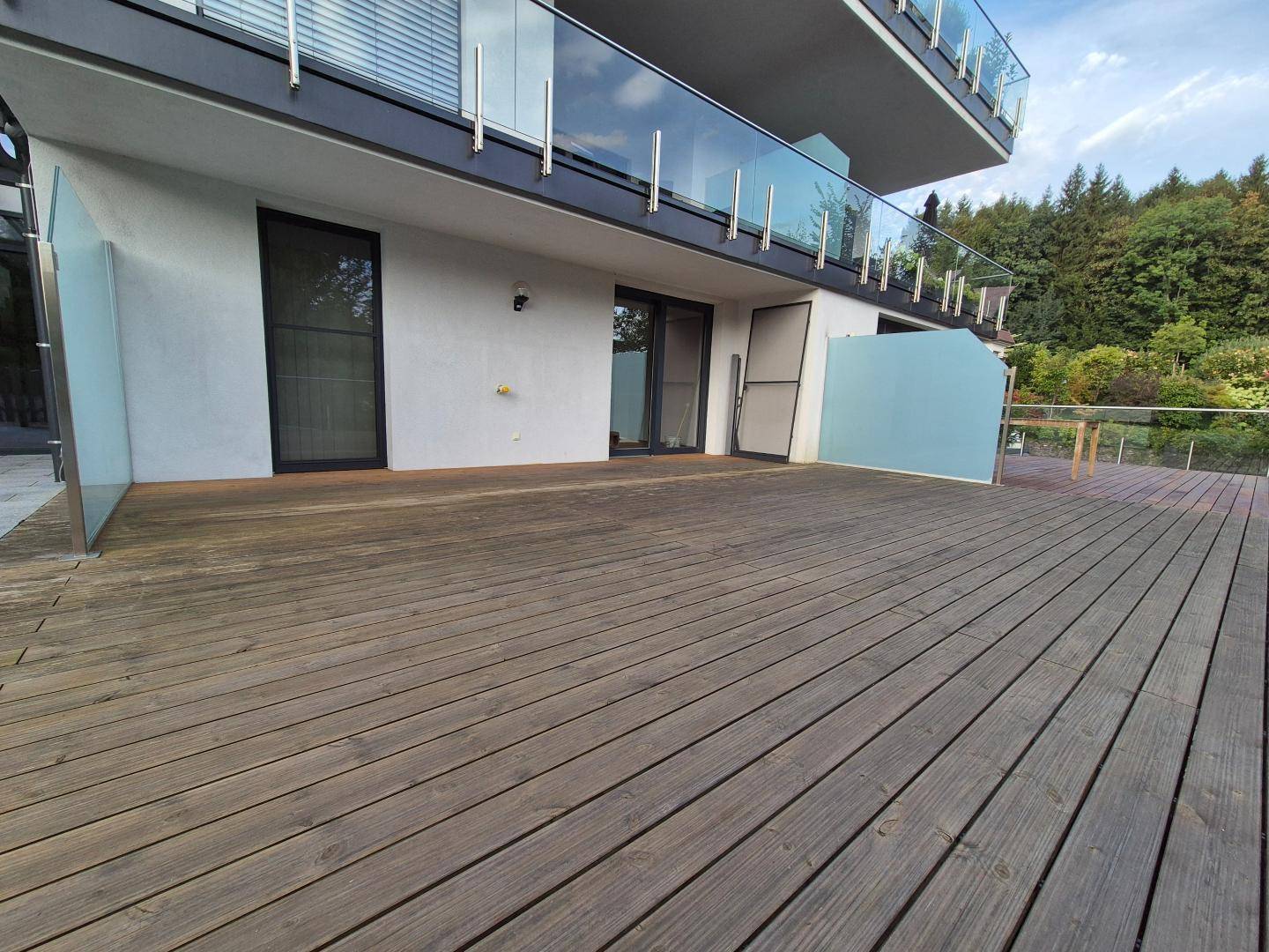 Große Holzterrasse vor einer modernen Gebäudefassade mit großen Fenstern und Balkonen.