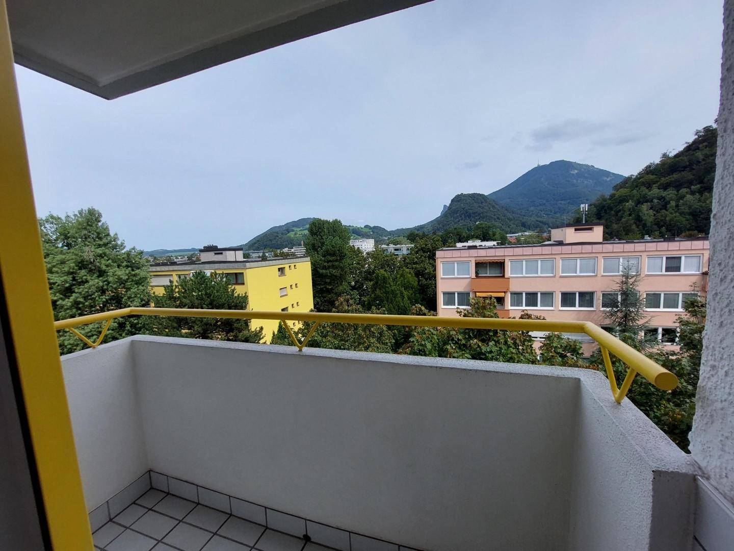Balkon mit gelbem Geländer und weitem Blick auf die Berge und umliegende Gebäude.