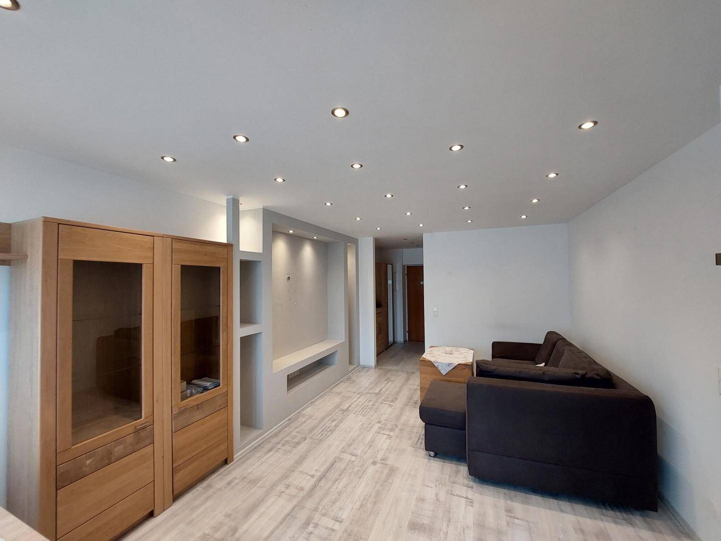 Gemütliches Wohnzimmer mit dunklem Ecksofa, Einbauregalen und hellem Laminatboden.