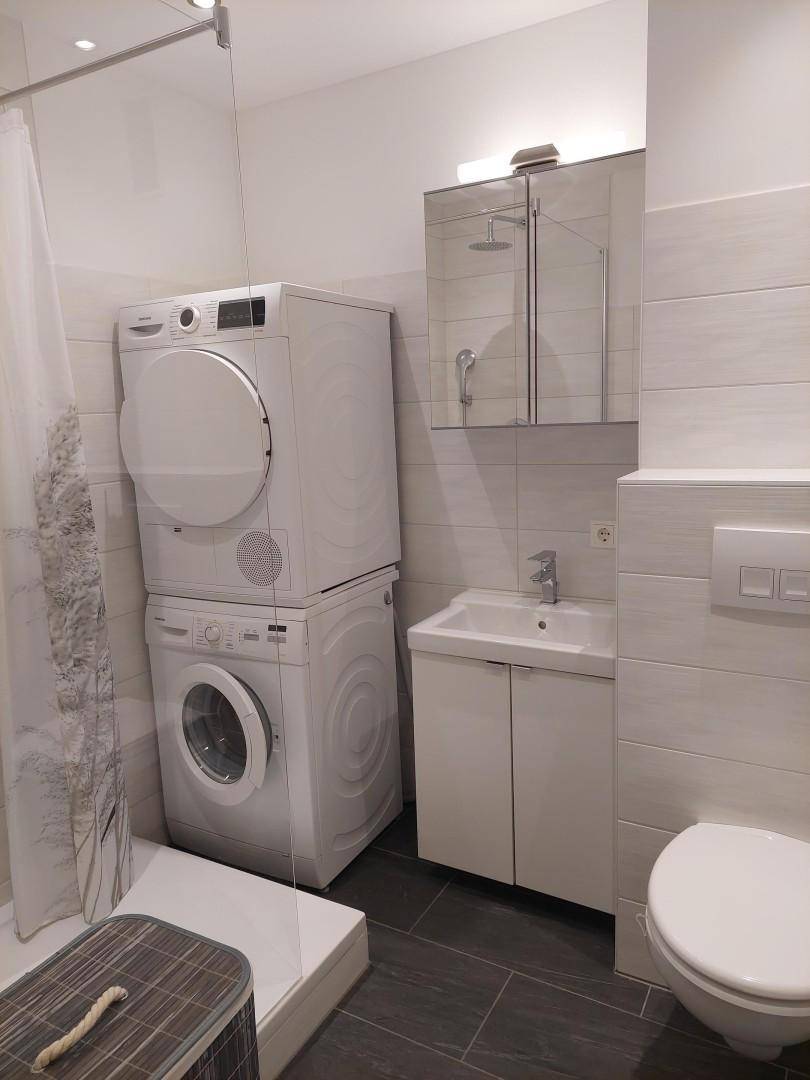 Modernes Badezimmer mit Dusche, Waschmaschine, Trockner und Spiegelschrank.