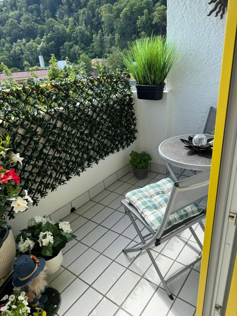 Gemütlicher Balkon mit Fliesenboden, Sitzgelegenheiten und vielen Pflanzen, umgeben von Grün.
