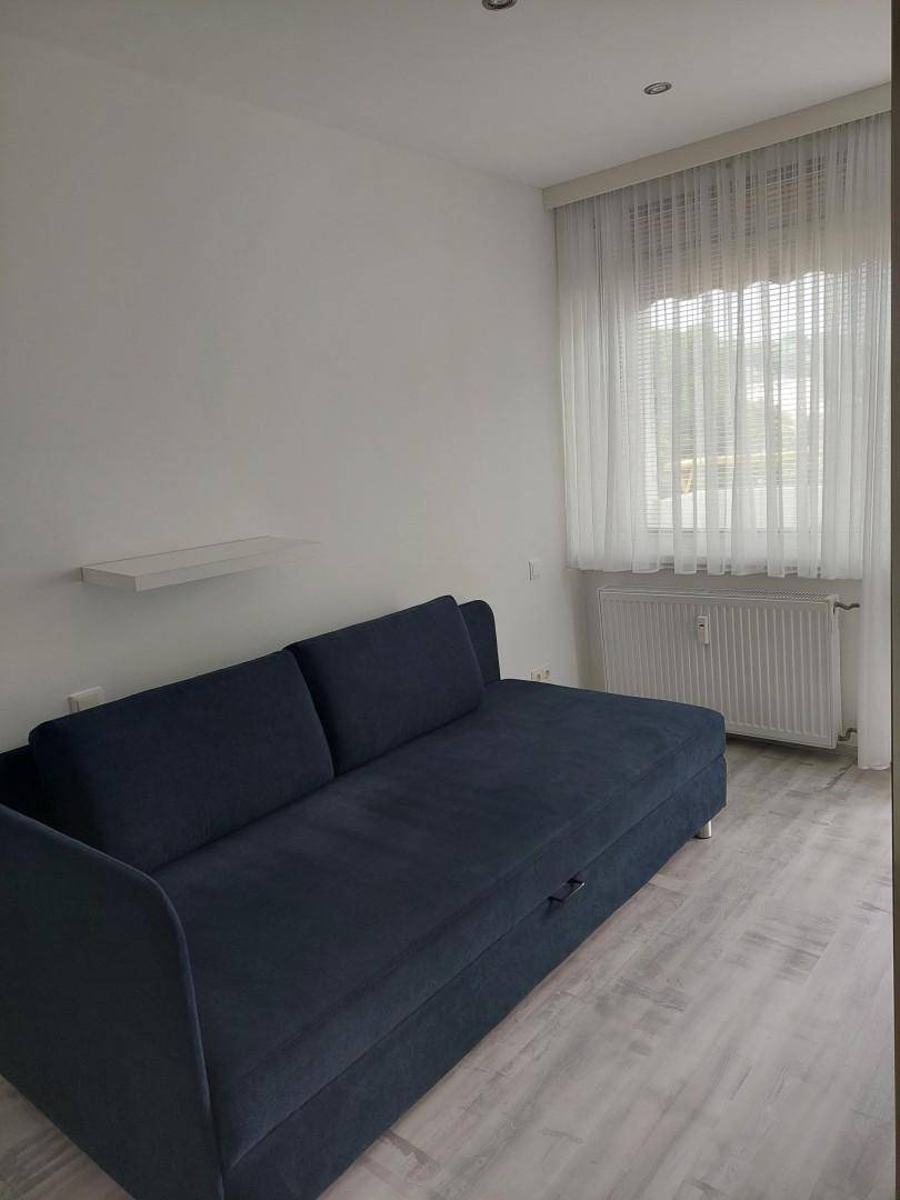 Helles Schlafzimmer mit Schlafsofa, Fenster und Heizkörper, ideal für Gäste oder als Arbeitszimmer.