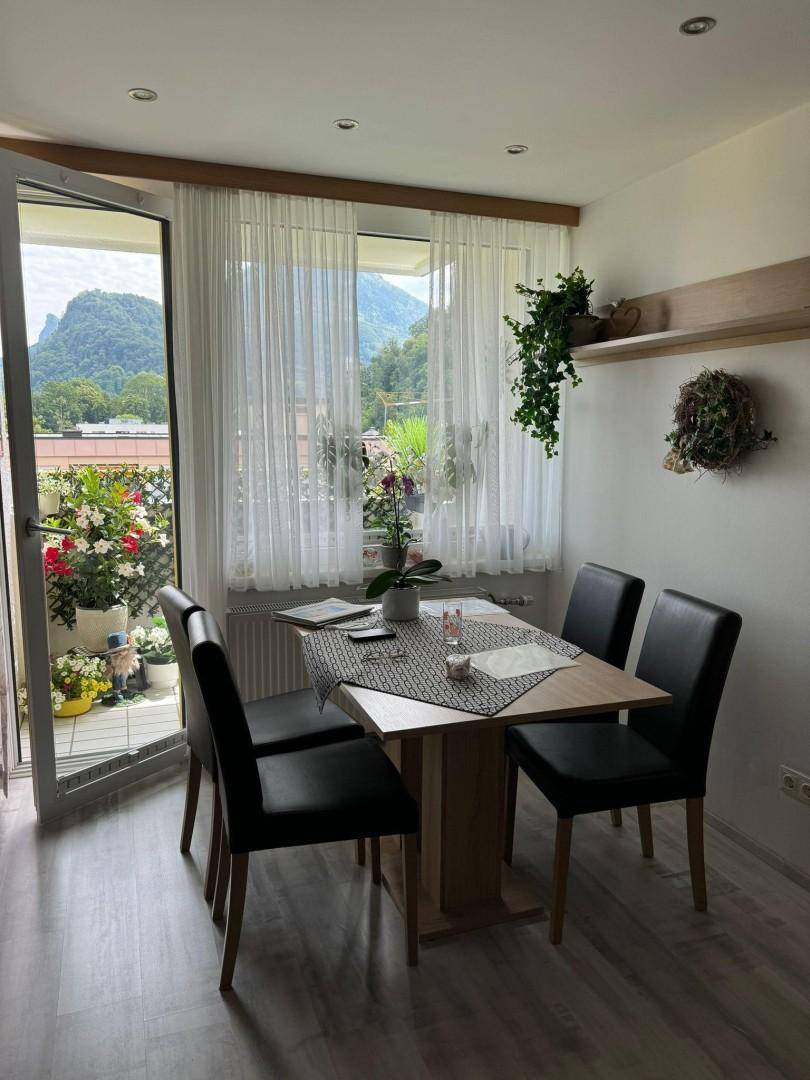 Heller Essbereich mit Tisch und Stühlen, direktem Zugang zum blühenden Balkon und Bergblick.
