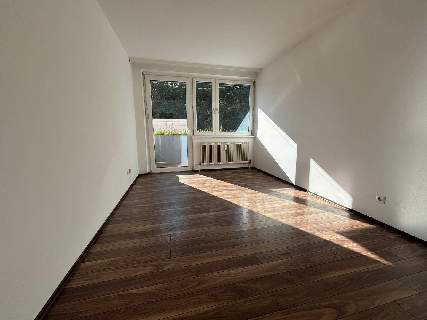 Heller Raum mit Holzboden und direktem Zugang zu einem Balkon oder einer Terrasse.