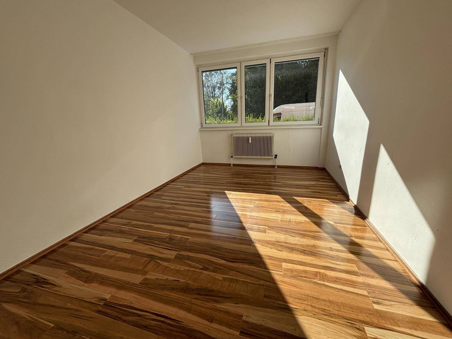 Lichtdurchfluteter Raum mit Holzboden und Blick ins Grüne durch die Fenster.