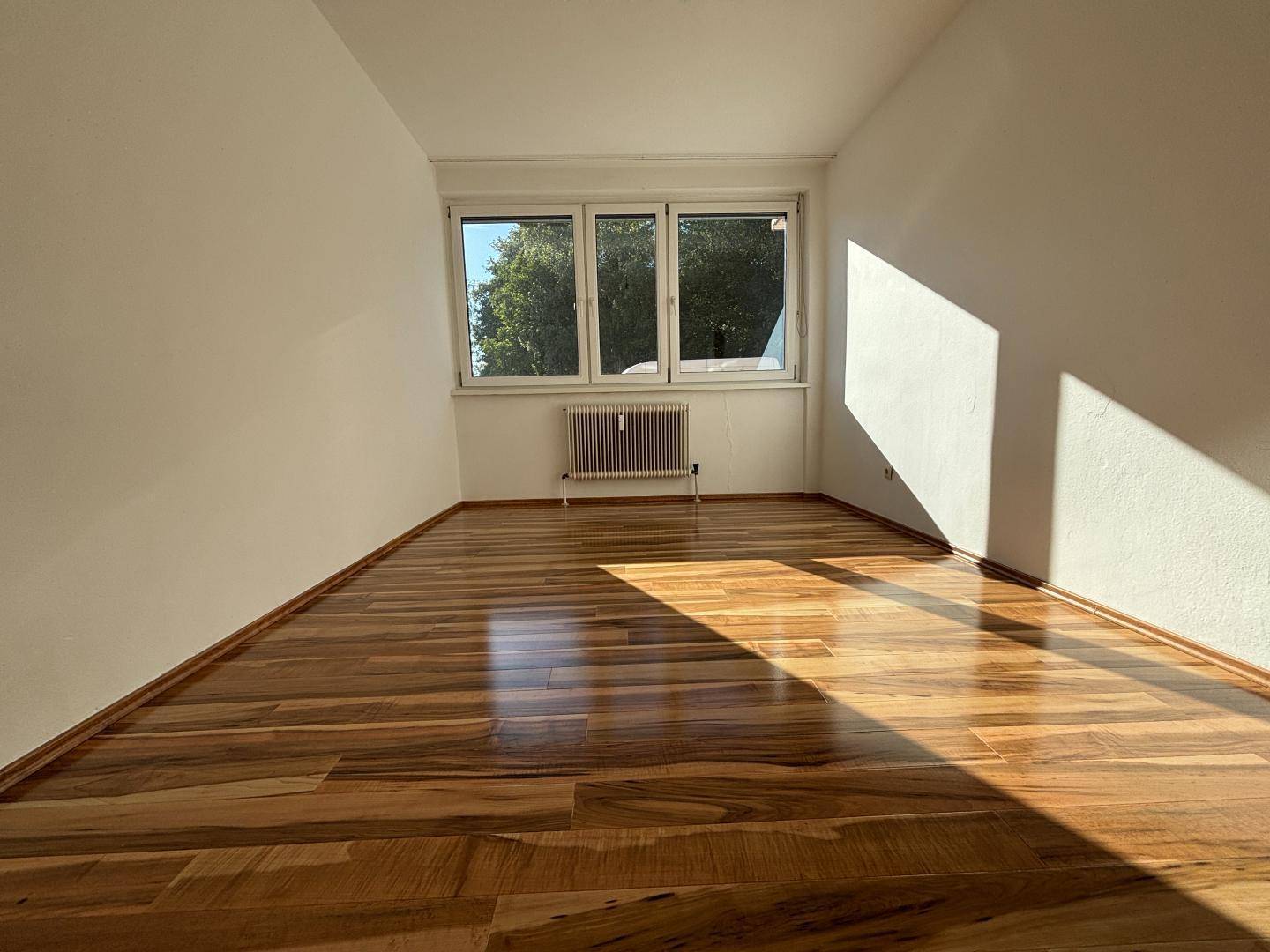 Heller Raum mit großen Fenstern, Holzboden und viel natürlichem Licht.