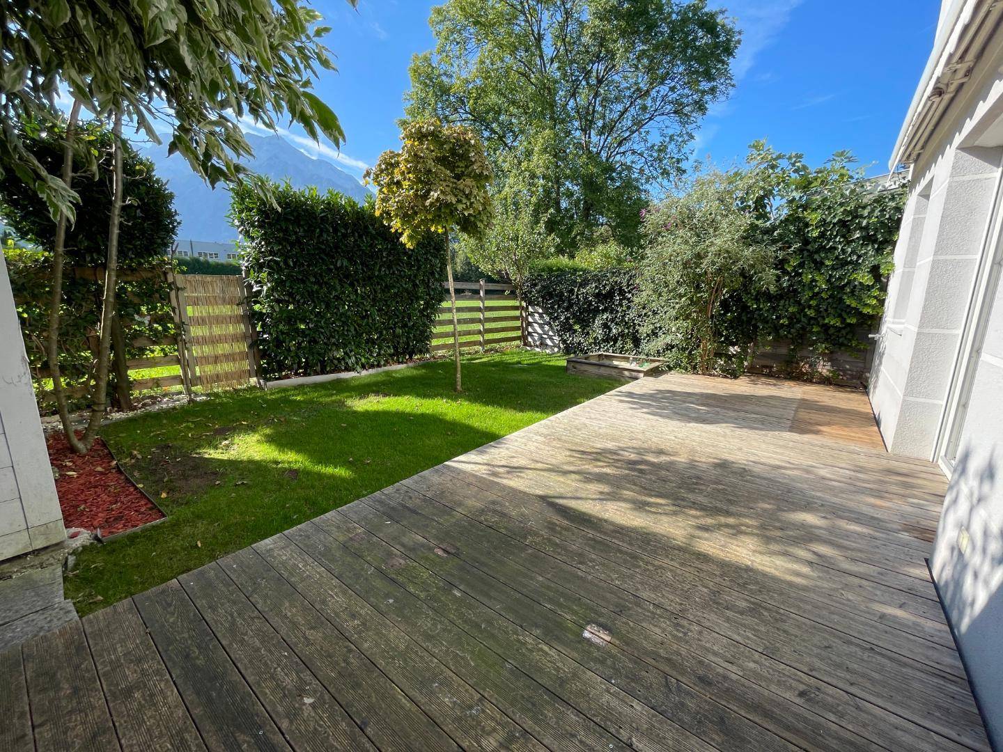 Gepflegter Gartenbereich mit Rasenfläche, Hecke und Holzterrasse.