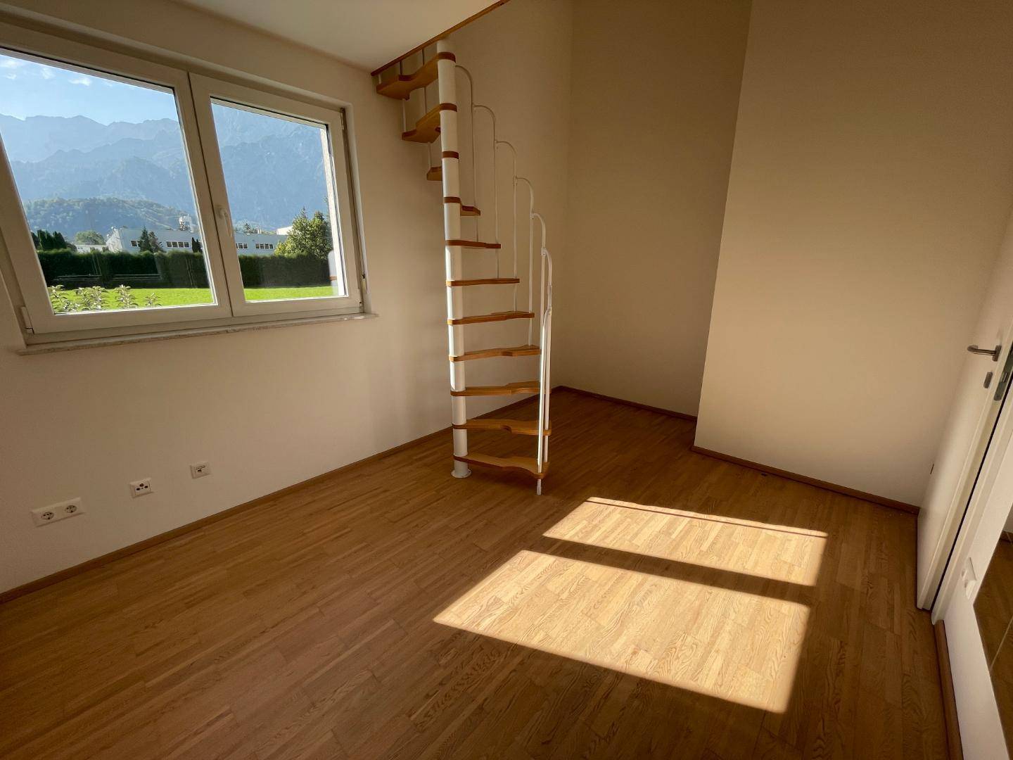 Helles Schlafzimmer mit Holztreppe und weitem Blick auf die Berge.