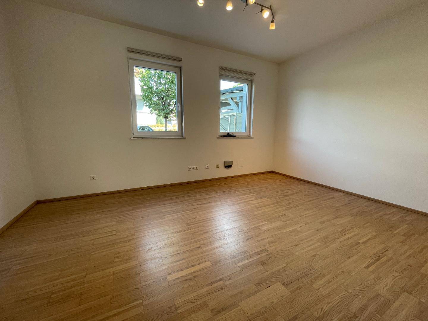 Heller Raum mit Parkettboden und zwei Fenstern, vielseitig nutzbar.