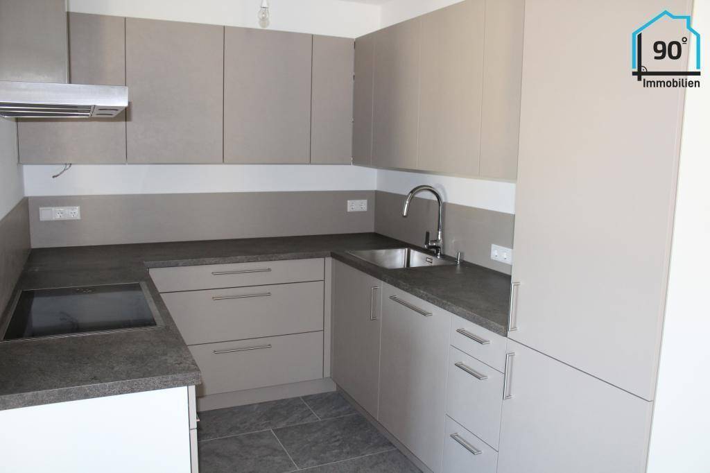 Moderne Einbauküche mit grauen Schränken, dunkler Arbeitsplatte und integriertem Kochfeld.